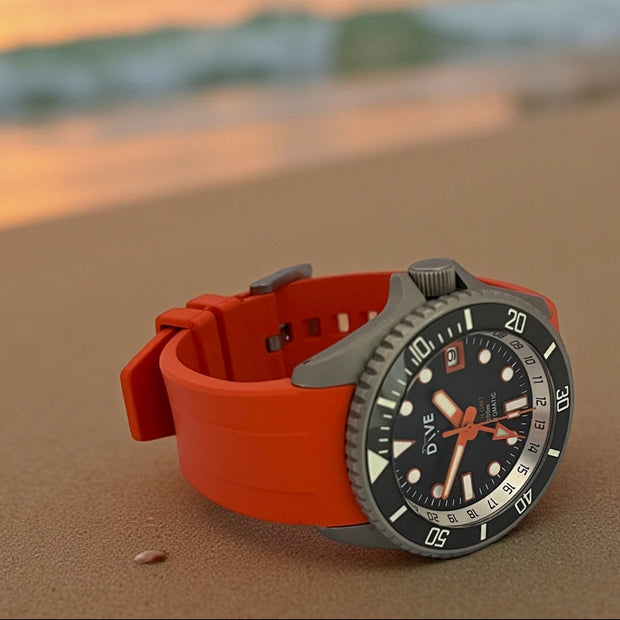 Dive watch with orange strap on a beach at sunset