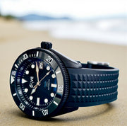HAND-BUILT DIVERS WATCH HADAL NOIR on a sandy beach, showcasing the bead blasted black PVD finish and stylish design.